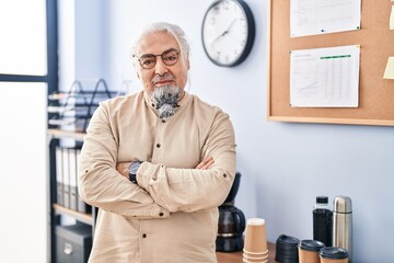 Middle age grey-haired man business worker standing with arms crossed gesture at office