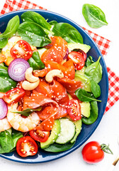 Fresh salad for keto diet with shrimp, salmon, avocado, spinach, cucumber, tomato, cashew nuts, sesame. Low-carbohydrate lunch rich in healthy fats. White table background, top view