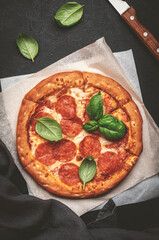 Pepperoni pizza with spicy salami sausage, mozzarella cheese, tomato sauce and green basil, black table background, top view