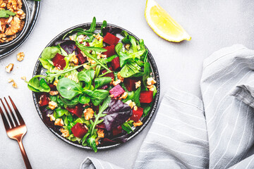 Beet salad with arugula, lettuce, chard and walnuts and lemon dressing, gray kitchen table, copy space. Fresh useful vegan dish for healthy eating