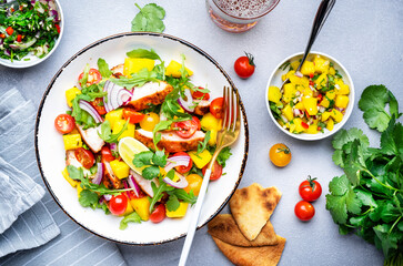 Fresh salad with grilled chicken and mango, salsa, tomatoes, cilantro, red onion and lettuce in tex-mex style, white table background, top view