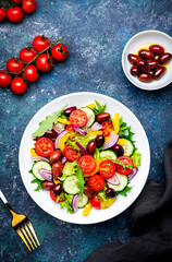 Tasty salad with kalamata olives, tomatoes, paprika, cucumber and onion, healthy mediterranean food. Blue table background, top view