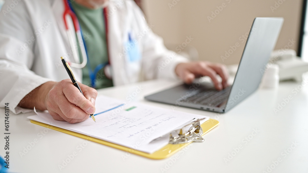 Sticker Middle age grey-haired man doctor using laptop writing medical report at clinic