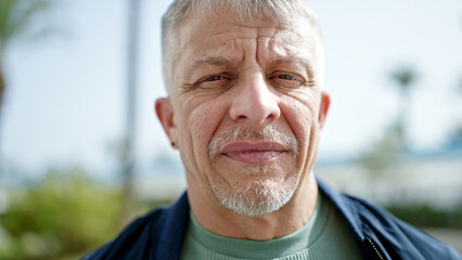 Middle age grey-haired man standing with serious expression at park