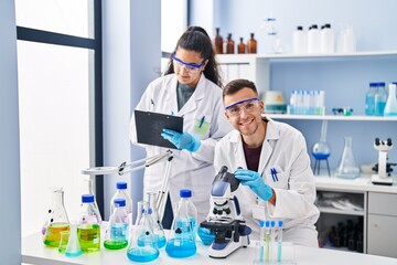 Fototapeta premium Man and woman wearing scientist uniform using microscope write on document at laboratory