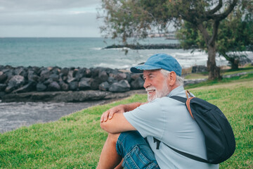 Side view portrait of senior relaxed man sitting on the meadow in front to the sea looking at horizon enjoying relax and retirement