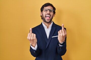 Handsome latin man standing over yellow background showing middle finger doing fuck you bad...