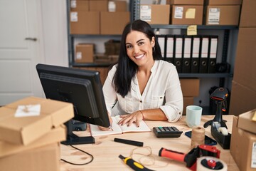 Young beautiful hispanic woman ecommerce business worker writing on notebook at office