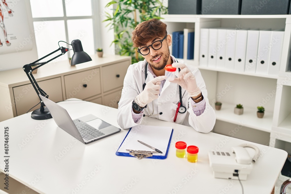 Poster Young arab man wearing doctor uniform analysing urine test tube speaking at clinic