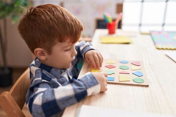 Adorable toddler playing with maths puzzle game sitting on table at classroom