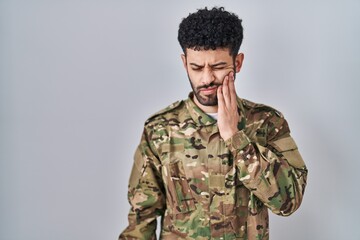 Arab man wearing camouflage army uniform touching mouth with hand with painful expression because...