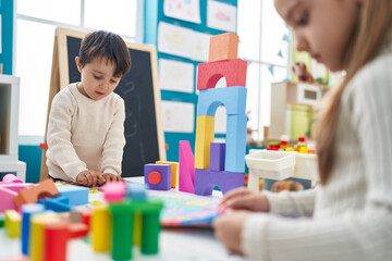 Adorable boy and girl playing with construction blocks and vocabulary puzzle at kindergarten