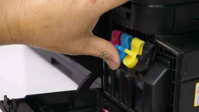 Hand holding blue ink cartridge inject printer at home office.  