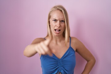 Young caucasian woman standing over pink background pointing displeased and frustrated to the camera, angry and furious with you