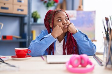 African american woman artist sitting on table with unhappy expression at art studio