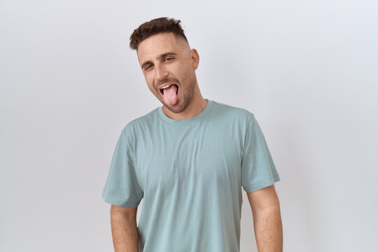 Hispanic man with beard standing over white background sticking tongue out happy with funny expression. emotion concept.