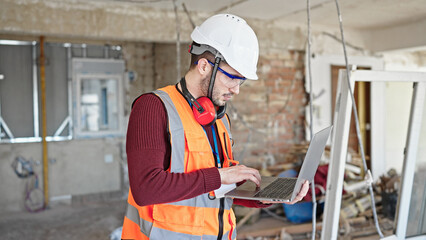 Young hispanic man builder using laptop at construction site