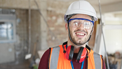 Young hispanic man builder smiling confident standing at construction site