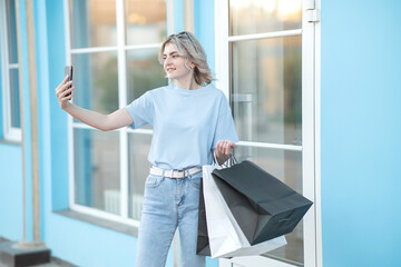 A girl in jeans with bags in her hands leaves the store in the summer.