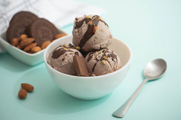 Chocolate ice cream decorated with nuts and chocolate icing, in a white bowl, blue background. Summer homemade cooling desserts