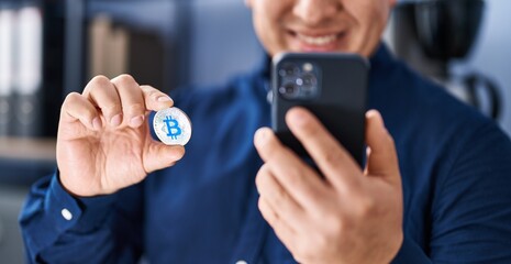 Young latin man business worker talking on smartphone holding bitcoin at office