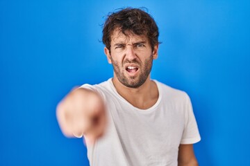 Hispanic young man standing over blue background pointing displeased and frustrated to the camera, angry and furious with you