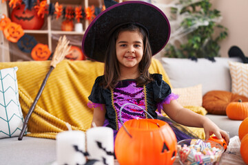 Adorable hispanic girl having halloween party holding pumpkin basket at home