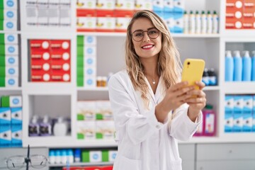 Young woman pharmacist smiling confident using smartphone at pharmacy