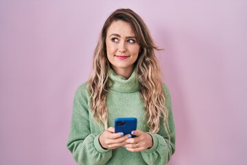 Young caucasian woman using smartphone typing message smiling looking to the side and staring away...
