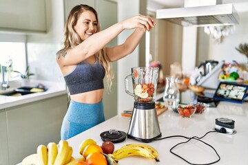 Young woman smiling confident pouring strawberries on blender at kitchen