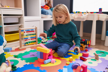 Fototapeta premium Adorable caucasian boy playing with car toy and construction blocks sitting on floor at kindergarten