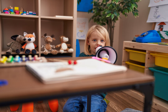 Adorable caucasian boy playing megaphone sitting on floor at kindergarten
