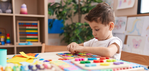 Adorable caucasian boy playing with maths puzzle game sitting on table at kindergarten