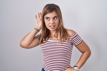 Young hispanic woman standing over isolated background smiling with hand over ear listening an hearing to rumor or gossip. deafness concept.