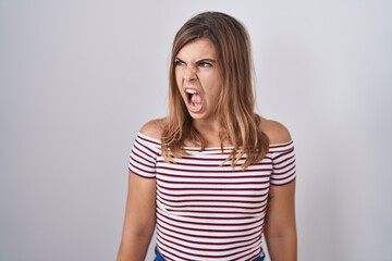 Young hispanic woman standing over isolated background angry and mad screaming frustrated and...