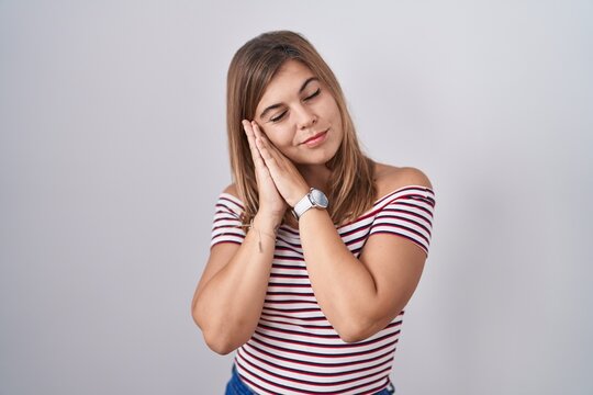 Young hispanic woman standing over isolated background sleeping tired dreaming and posing with hands together while smiling with closed eyes.