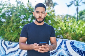 Young latin man using smartphone with serious expression at park