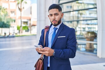 Young latin man business worker using smartphone with serious expression at street