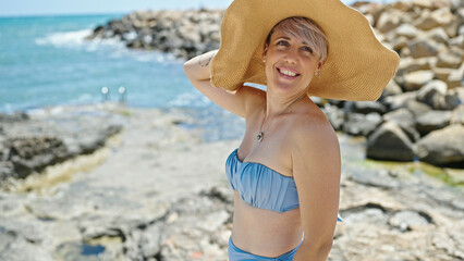 Young woman tourist wearing bikini and summer hat smiling at beach