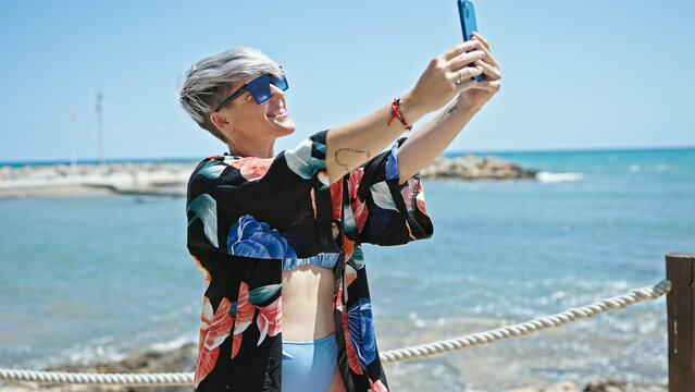 Young woman tourist wearing bikini and sunglasses make selfie by smartphone at beach