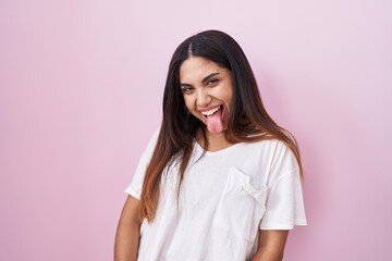 Fototapeta premium Young arab woman standing over pink background sticking tongue out happy with funny expression. emotion concept.