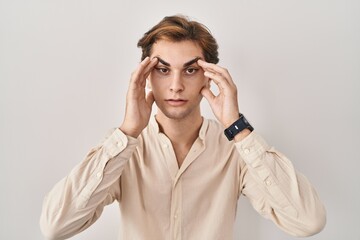 Young man standing over isolated background trying to open eyes with fingers, sleepy and tired for morning fatigue