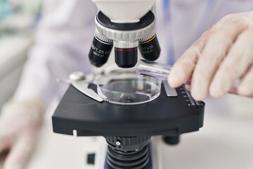 Young caucasian man scientist using microscope pouring liquid on sample at laboratory