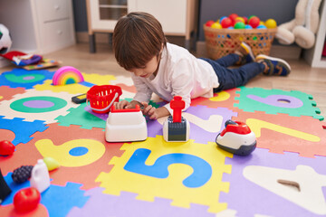 Adorable caucasian boy playing with supermarket toy lying on floor at kindergarten