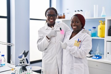 Two african women working at scientist laboratory smiling happy pointing with hand and finger