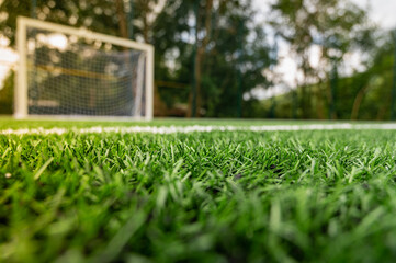 Morning sunrise, corner of a soccer field goal with white markers, on an artificial green surface - obrazy, fototapety, plakaty