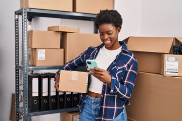 African american woman ecommerce business worker using smartphone holding package at office