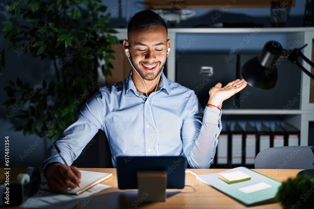 Canvas Prints young hispanic man working at the office at night smiling cheerful presenting and pointing with palm