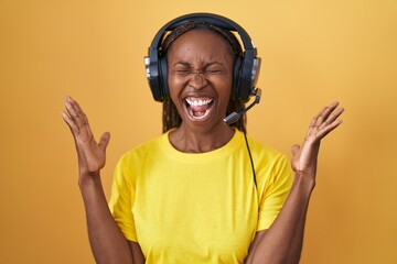 African american woman listening to music using headphones celebrating mad and crazy for success with arms raised and closed eyes screaming excited. winner concept