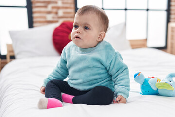 Adorable hispanic baby sitting on bed with relaxed expression at bedroom